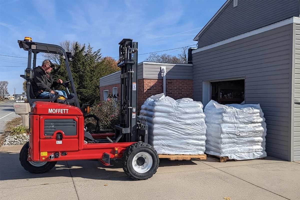 A Moffett piggyback forklift lowering a wood pellet skid onto a residential driveway