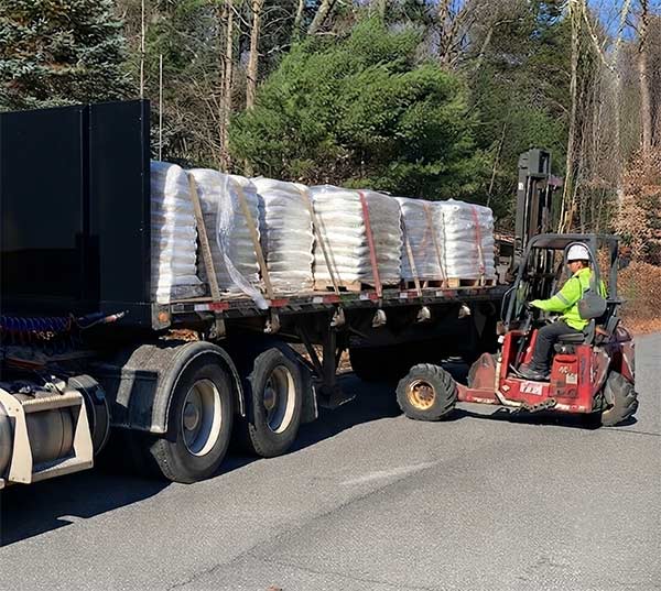 A Moffett piggyback forklift offloading a shrink-wrapped skid of wood pellets from a delivery truck