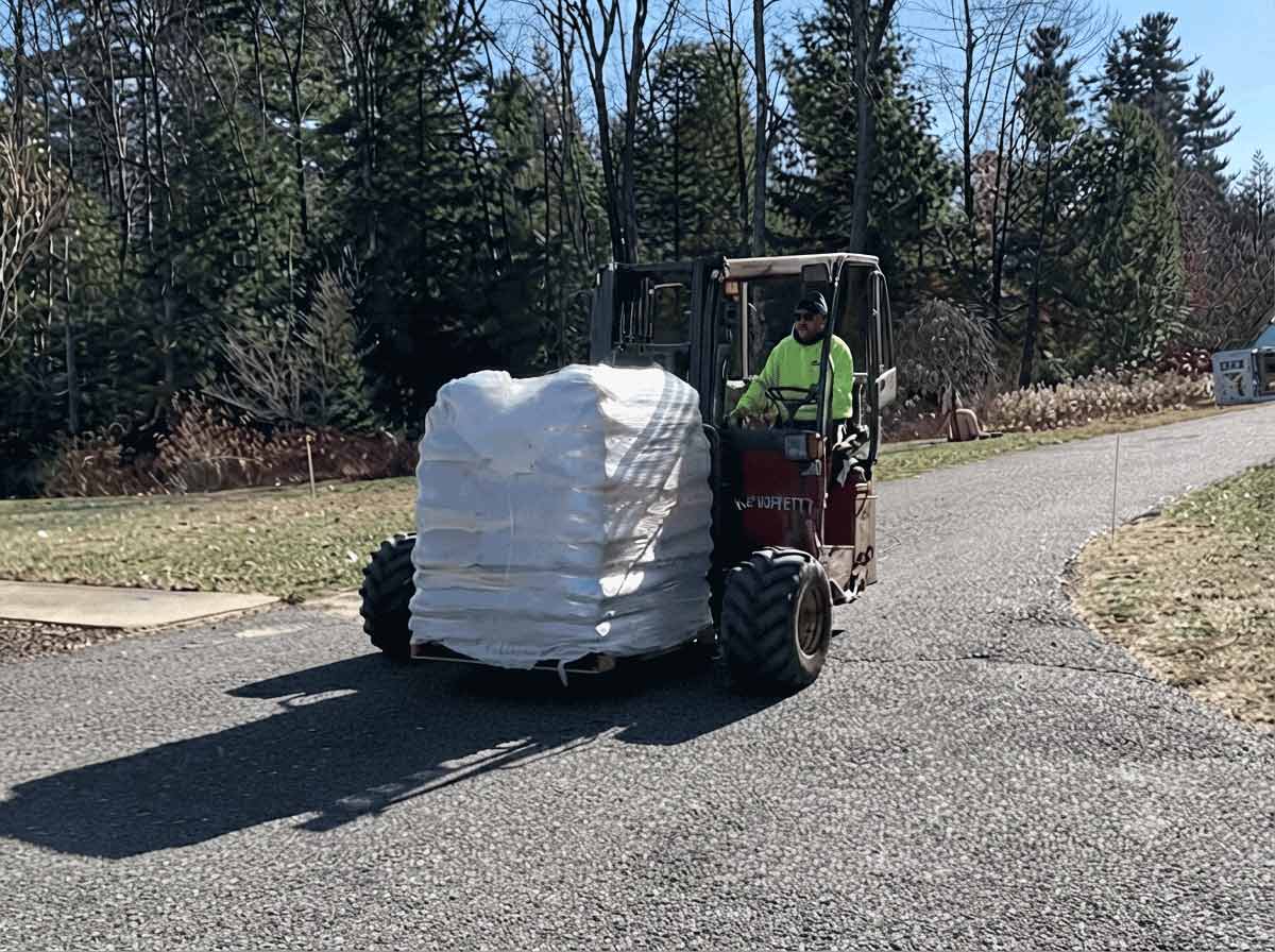 Piggyback forklift delivering a shrink-wrapped pallet of wood pellets down a driveway