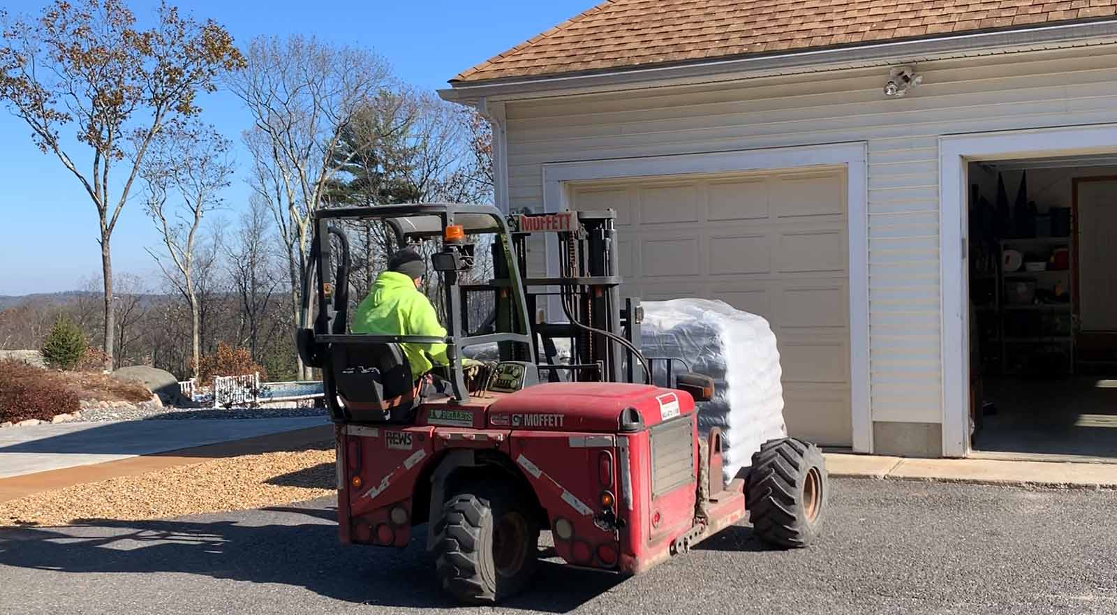 Forklift delivering a pallet of wood pellets to a home garage